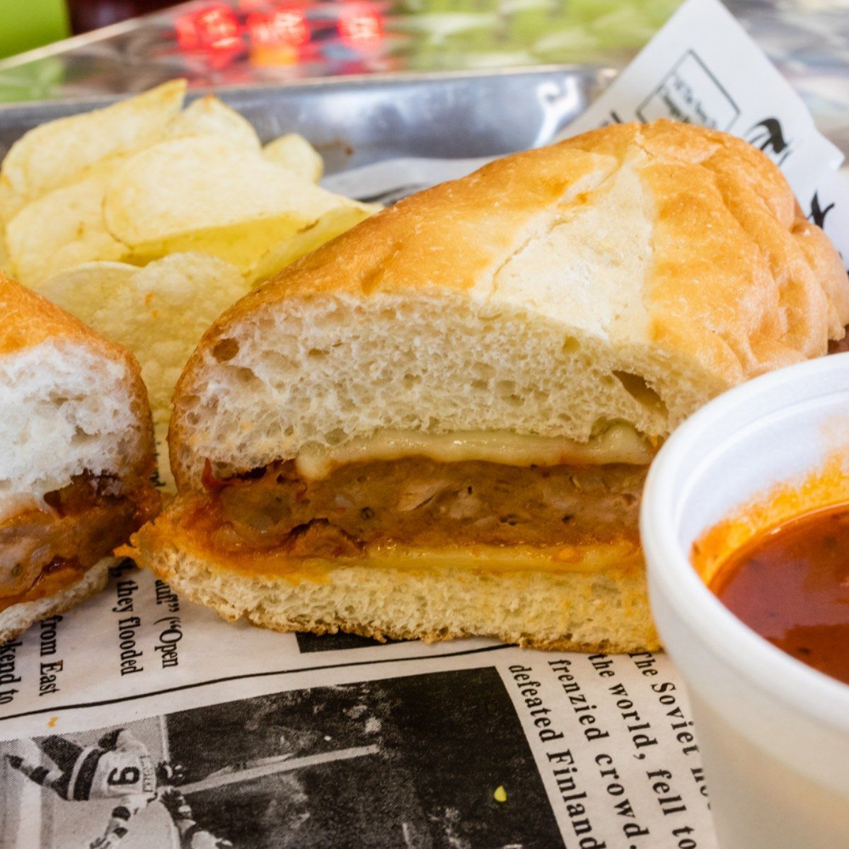 A sandwich on a newspaper with a cup of soup