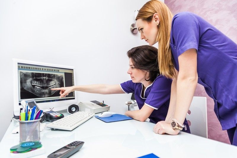 Two people reviewing dental X-rays on a monitor in a clinic office, one pointing at the screen.
