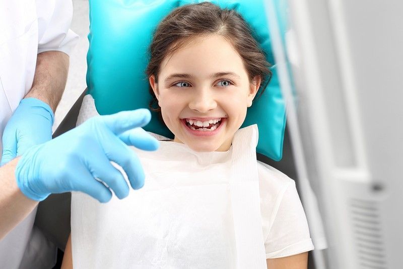 Child brushing teeth with a blue toothbrush, smiling in a bright bathroom setting