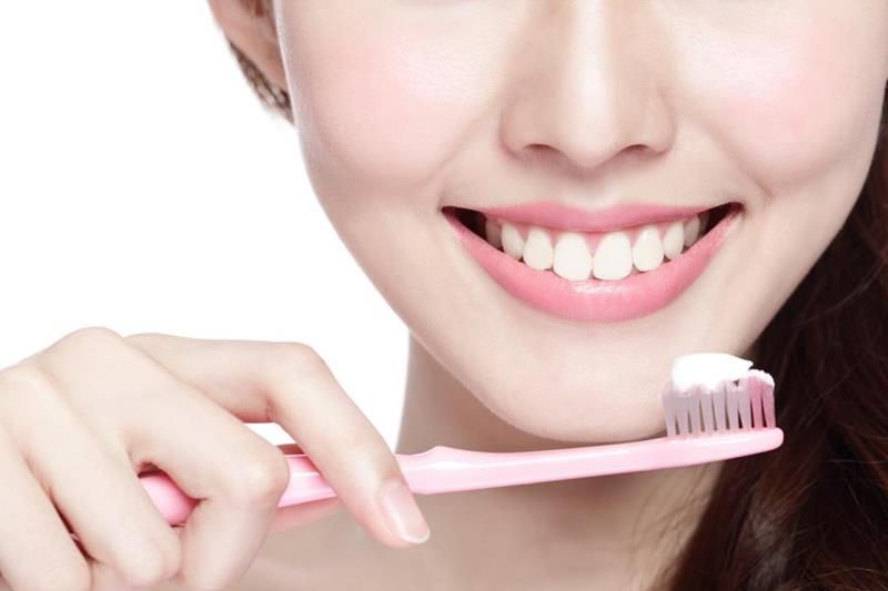 Smiling person brushing teeth with a pink toothbrush and toothpaste