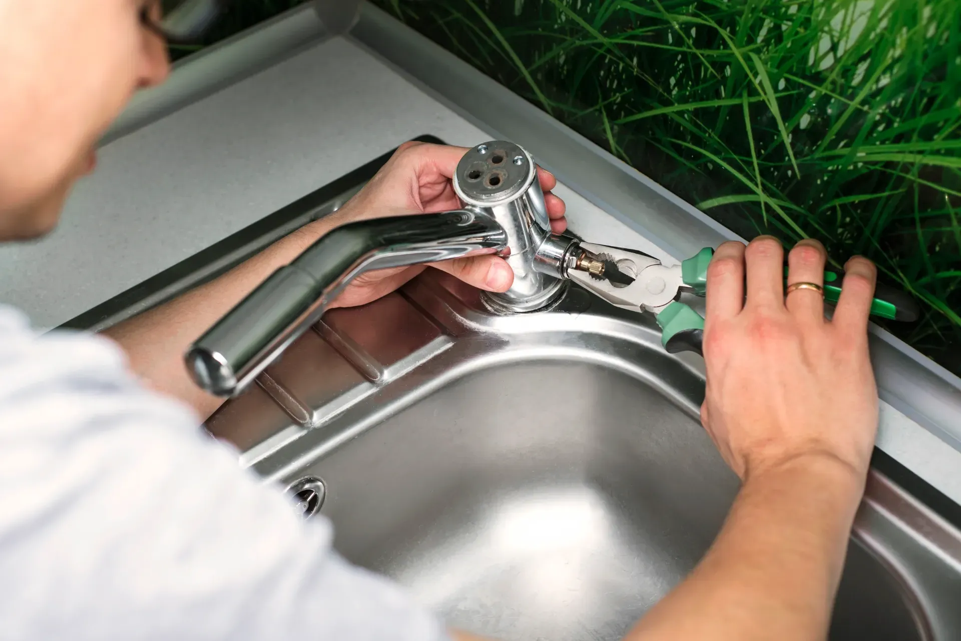Person fixing a kitchen faucet at a stainless steel sink with a wrench — New Gen Plumbing and Gas in Pottsville, NSW