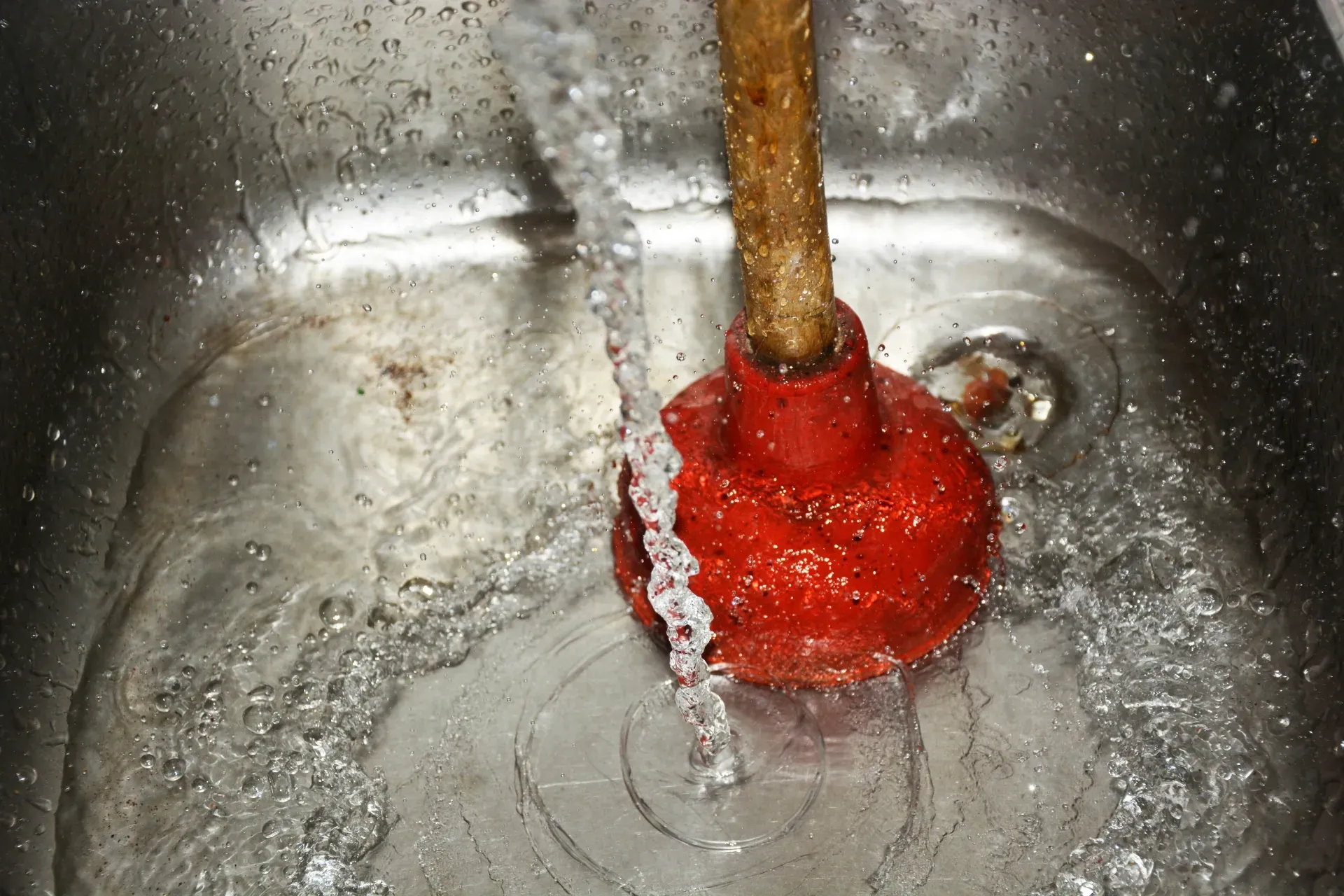 Red plunger in a stainless steel sink draining water around it — New Gen Plumbing and Gas in Banora Point, NSW