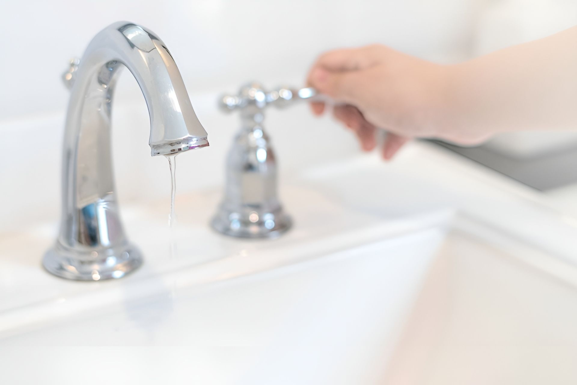 Hand Turning a Chrome Bathroom Faucet on a White Sink — New Gen Plumbing and Gas in Banora Point, NSW