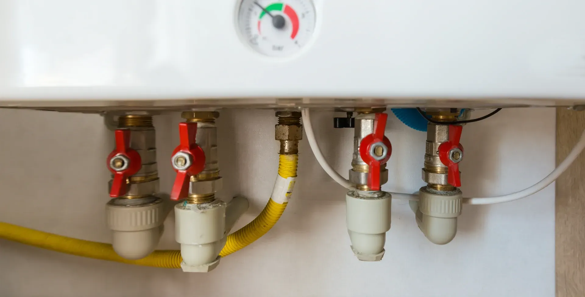Boiler underside with red valves and connected pipes, including yellow gas tubing. — New Gen Plumbing and Gas in Coolangatta, NSW