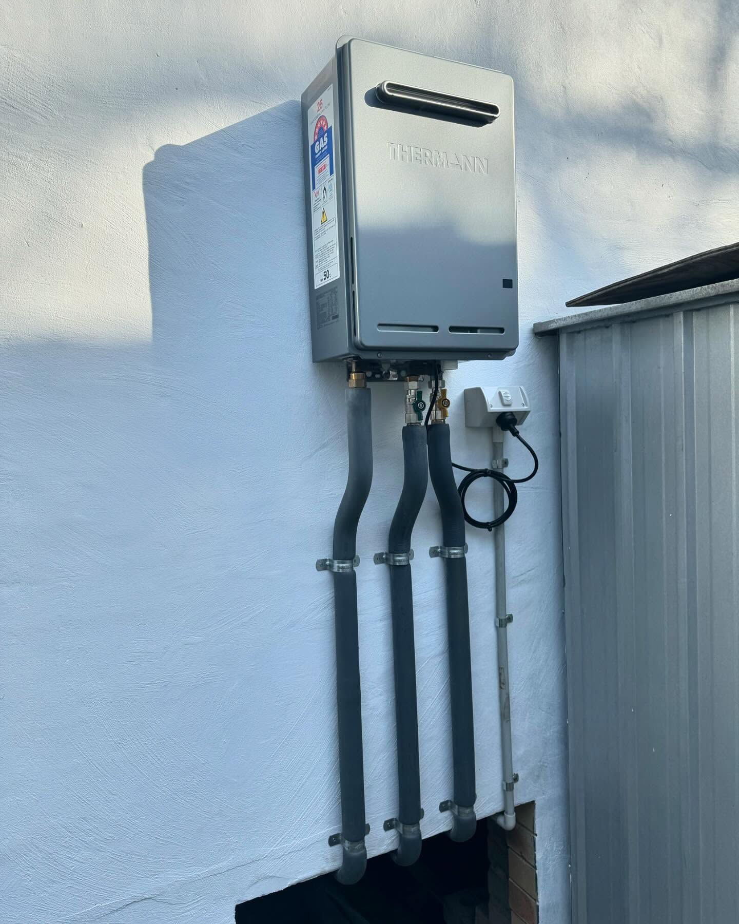 Exterior Wall-mounted Gas Water Heater With Three Gray Pipes and a Hose Loop — New Gen Plumbing and Gas in Banora Point, NSW