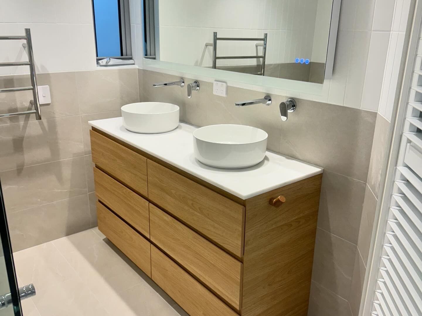 Modern bathroom vanity with wood drawers, white countertop, double sinks, and wall mirror by tiled wall — New Gen Plumbing and Gas in Kingscliff, NSW