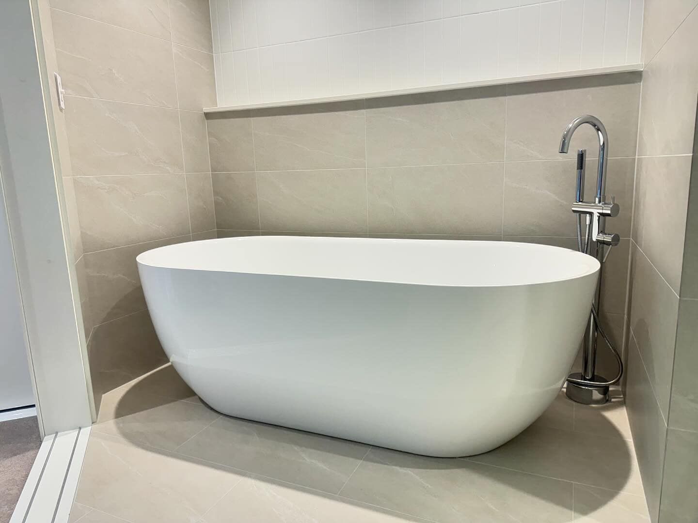 Modern white freestanding bathtub in a beige bathroom corner with chrome faucet — New Gen Plumbing and Gas in Banora Point, NSW