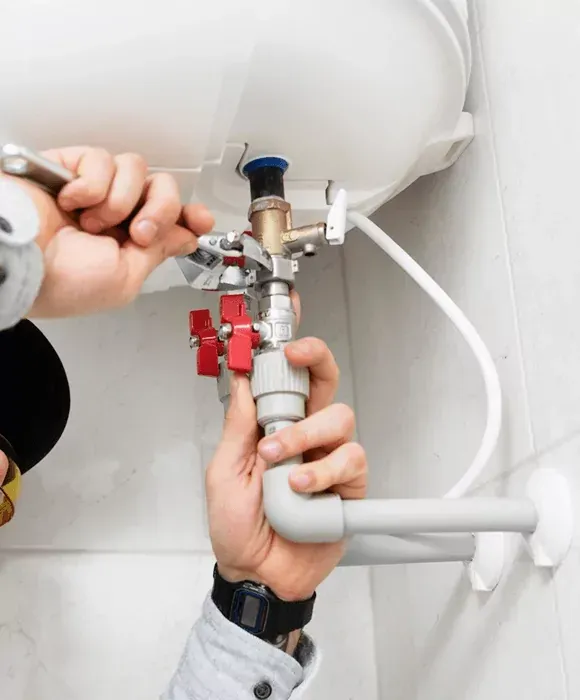 Plumber tightening valves under a sink with a wrench, repairing white pipes and red shutoff valves — New Gen Plumbing and Gas in Kingscliff, NSW