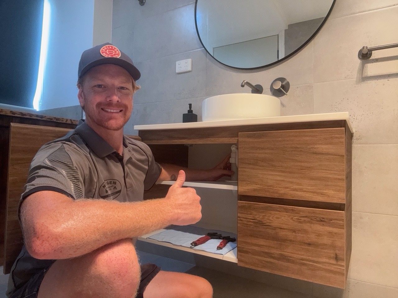 Man Smiling and Giving a Thumbs-up Beside a Wooden Bathroom Vanity — New Gen Plumbing and Gas in Banora Point, NSW