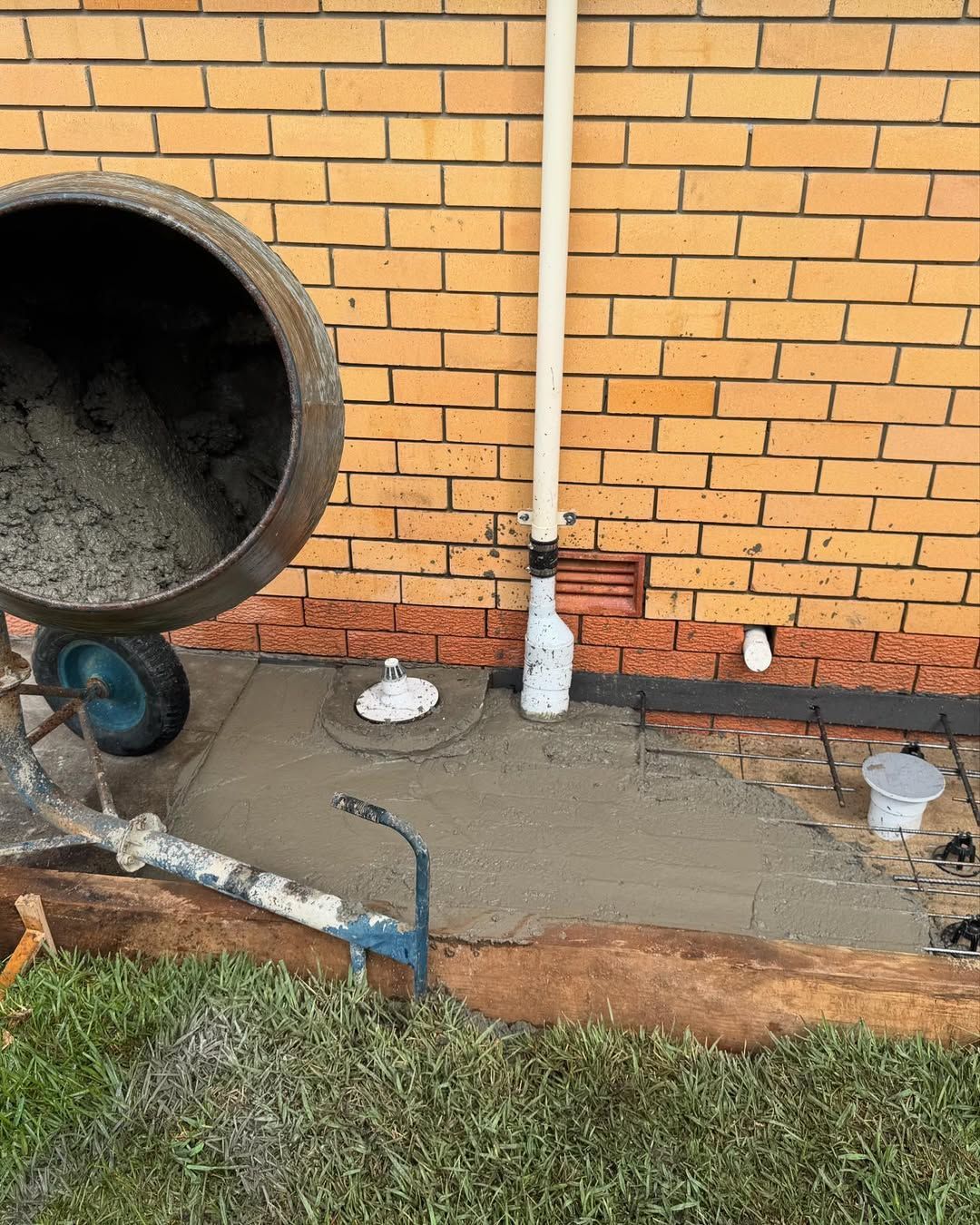 Concrete pad beside brick wall with large drain pipe and plumbing fittings, partly covered by wet cement. — New Gen Plumbing and Gas in Coolangatta, NSW
