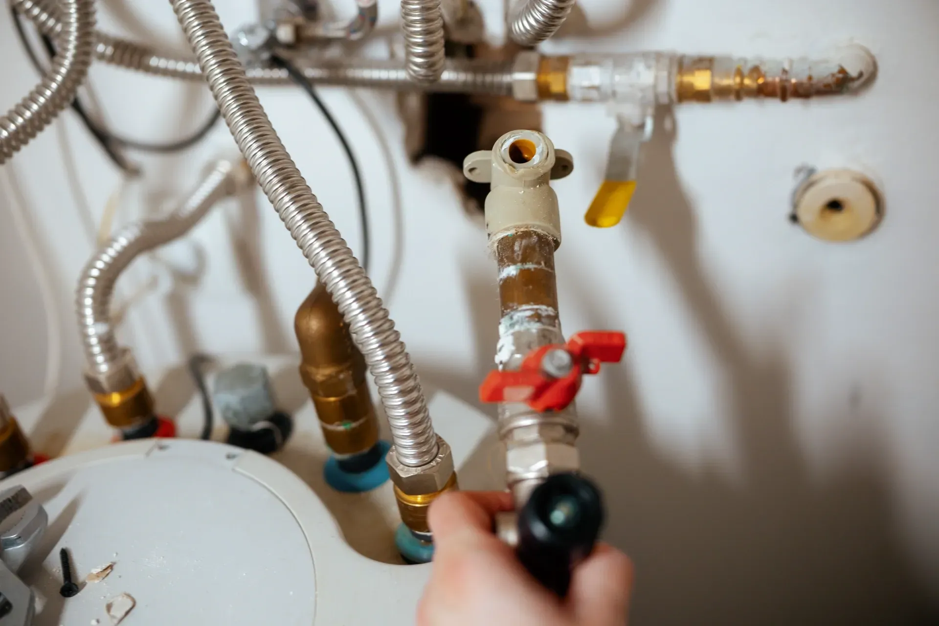 Hand holding a wrench near a red valve on exposed plumbing under a sink — New Gen Plumbing and Gas in Banora Point, NSW