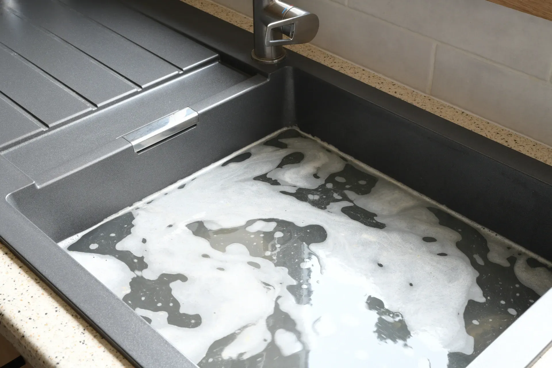 Soap-covered sink with gray metal basin and faucet, showing suds and dirty water pooling inside — New Gen Plumbing and Gas in Kingscliff, NSW