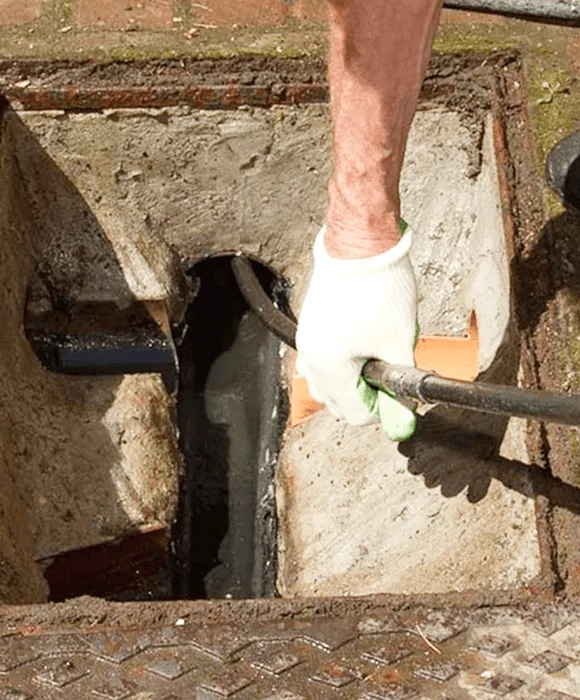 Gloved hand using a pipe in a concrete pit opening with rusted metal edges — New Gen Plumbing and Gas in Coolangatta, NSW