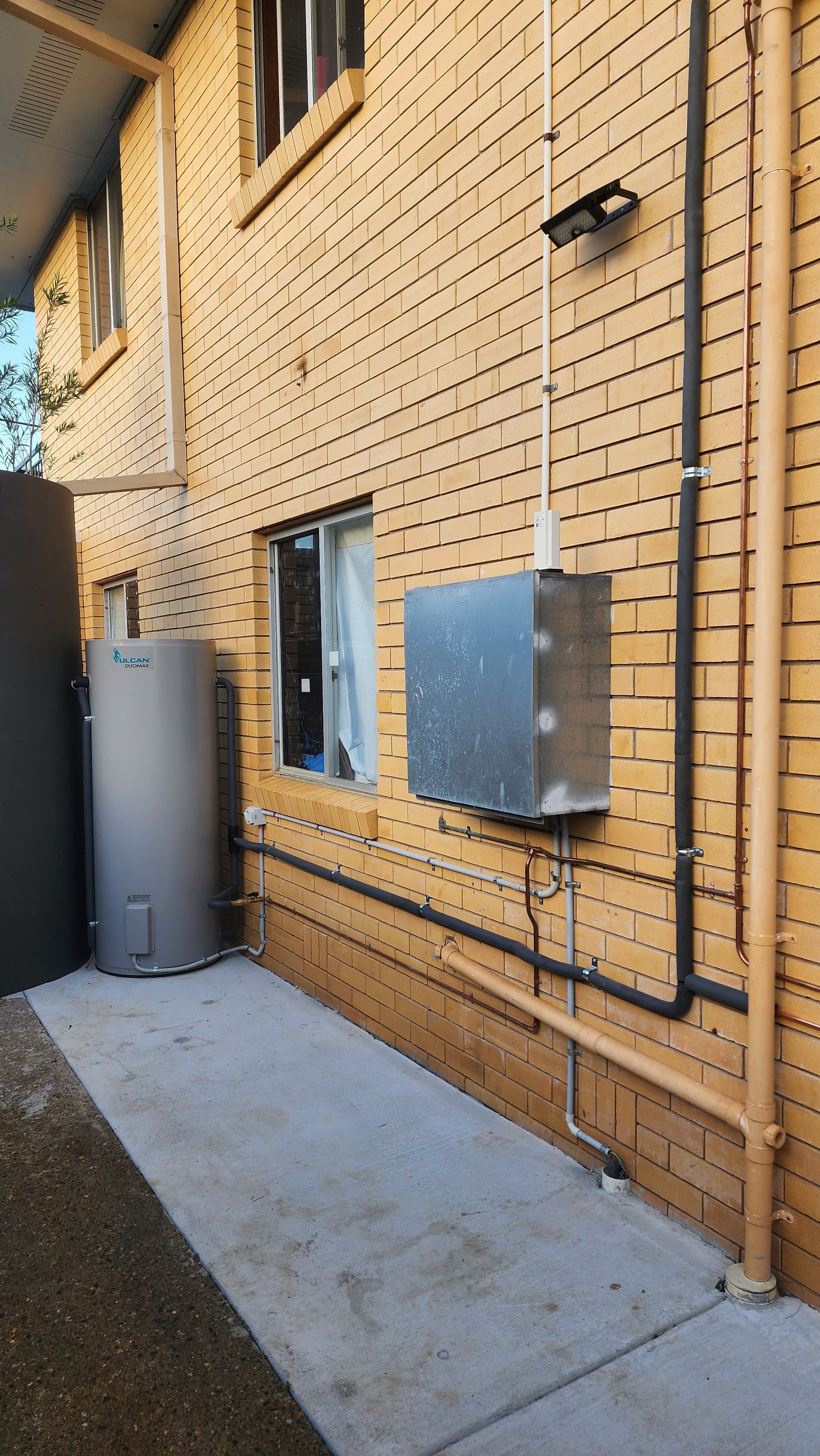Brick Building Exterior With Utility Boxes, Pipes, and a Tall Gray Tank — New Gen Plumbing and Gas in Murwillumbah, NSW