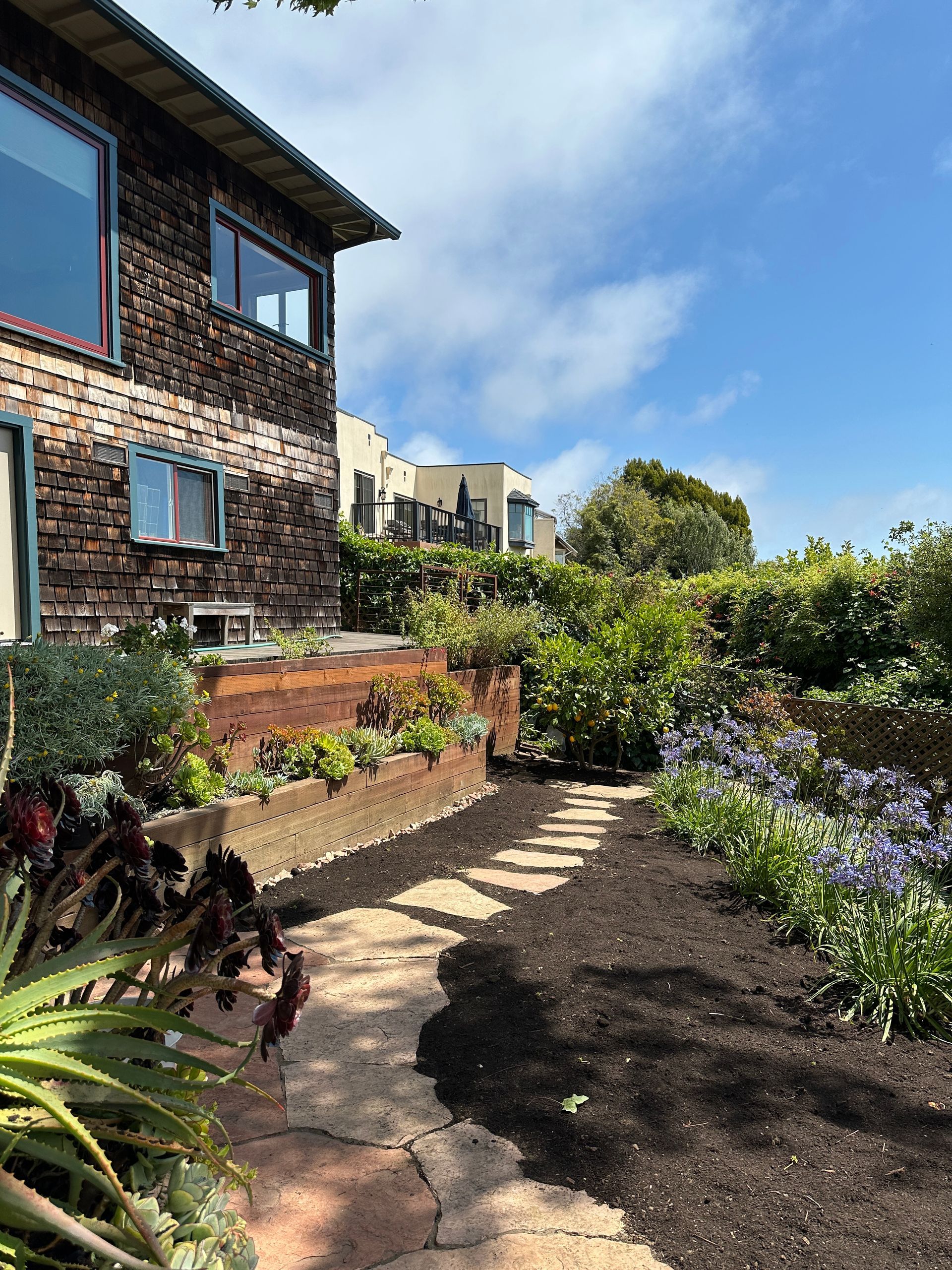 Stone path through a garden with a two-story house, sunny sky.