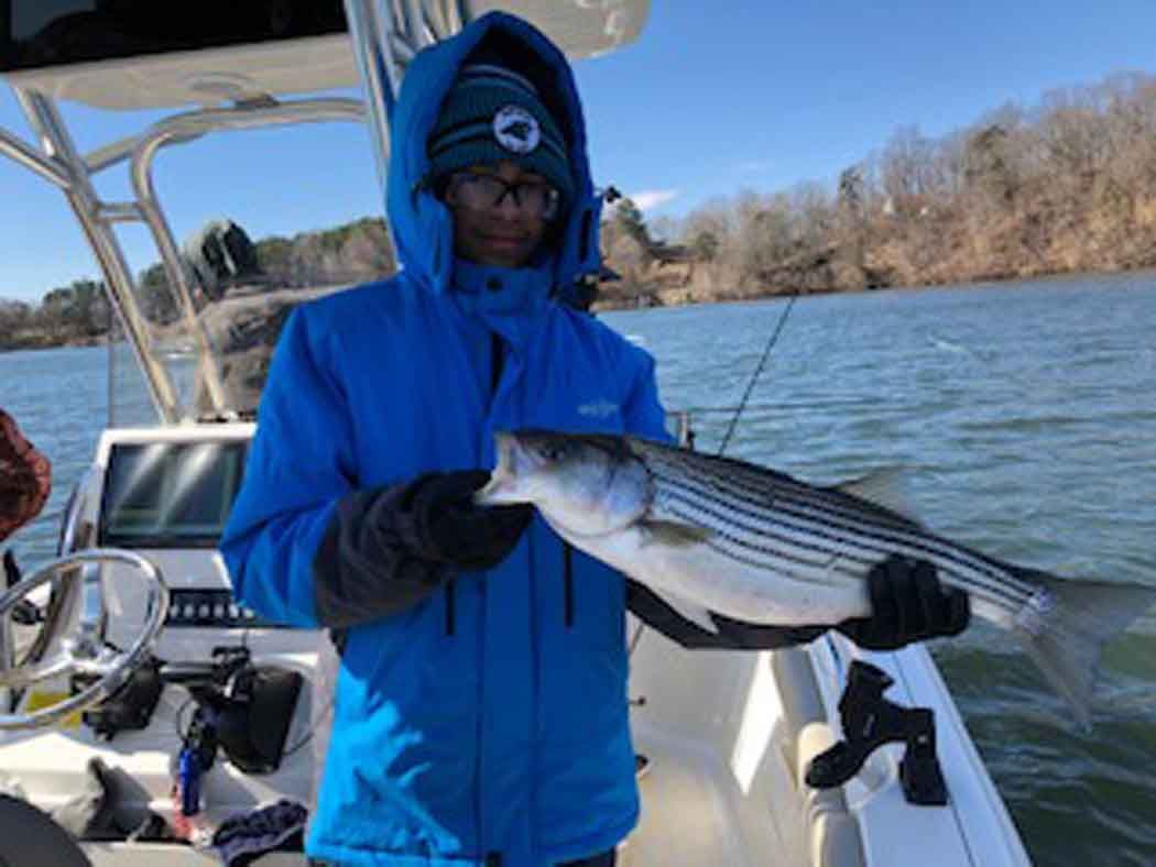 Person in blue jacket holding a striped fish on a boat on the water