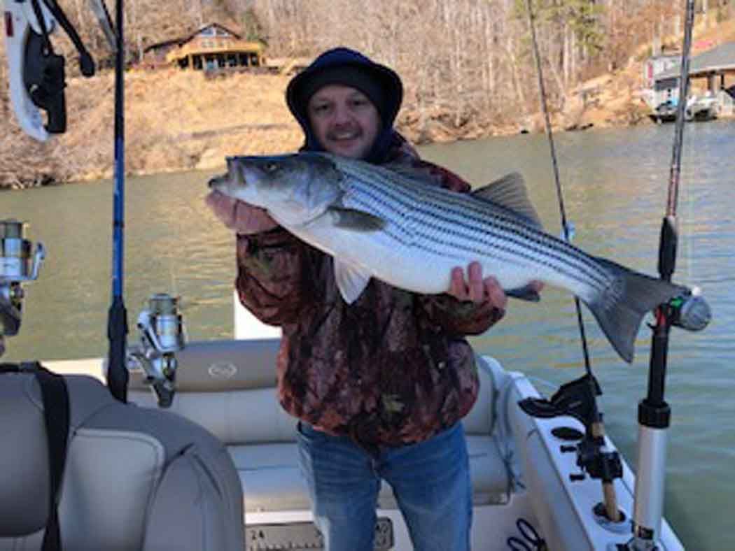 Person on a boat holding a large striped fish on a lake