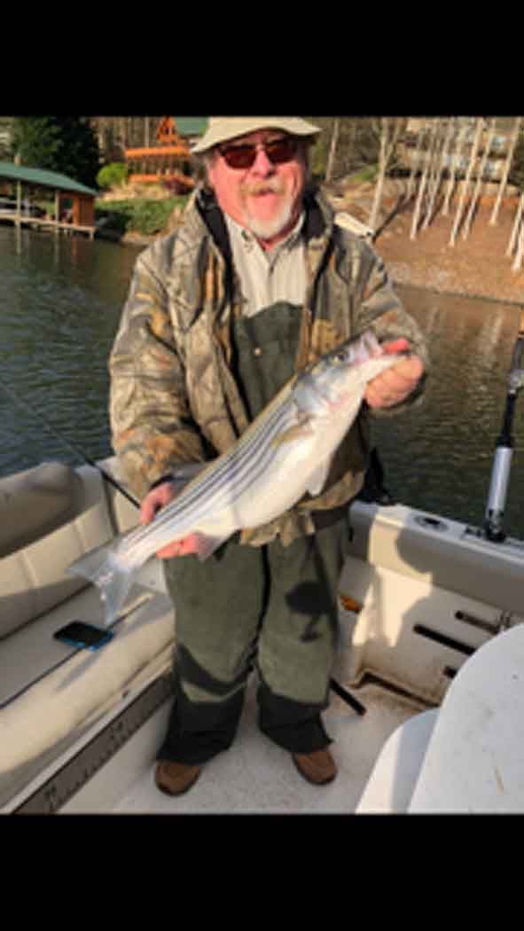 Angler on a boat holding a large silver fish on a calm lake
