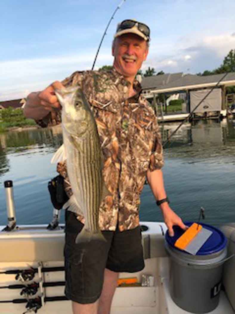 Man on a boat holding a large striped fish by the water at sunset