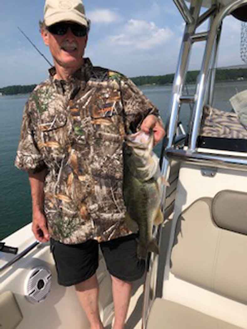 Person on a boat holding up a large fish on a sunny lake