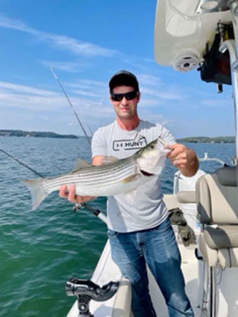 Man holding a striped fish on a boat on calm water under a blue sky