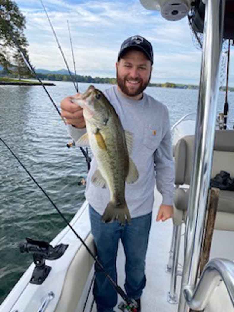 Smiling angler on a boat holding a large fish over calm water
