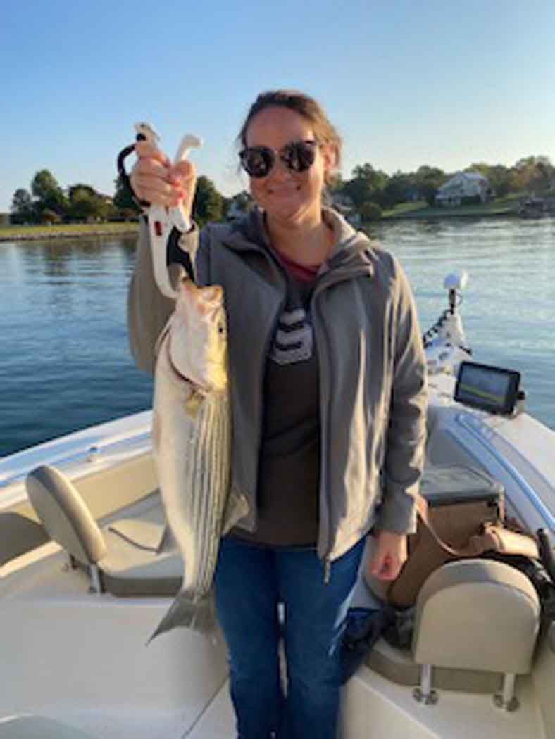Person on a boat holding up a large striped fish on a sunny lake