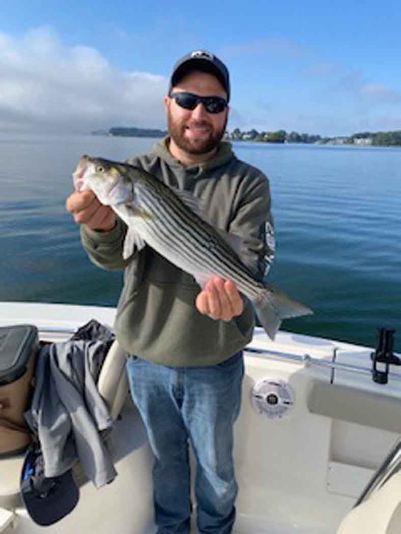 Man on a boat holding a large striped fish on a calm blue bay
