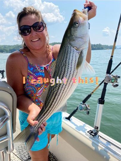 Woman on a boat holding a large striped fish, smiling on a sunny day.