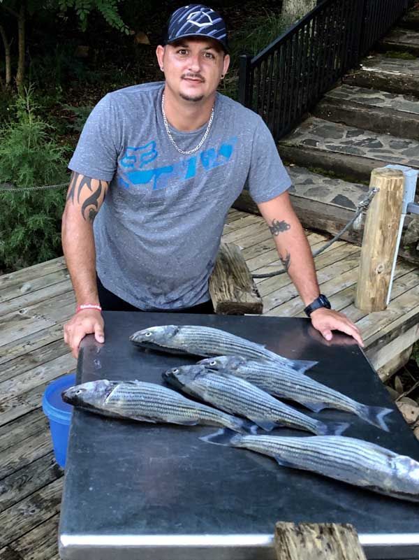Man posing behind four fish on a table outdoors near wooden steps