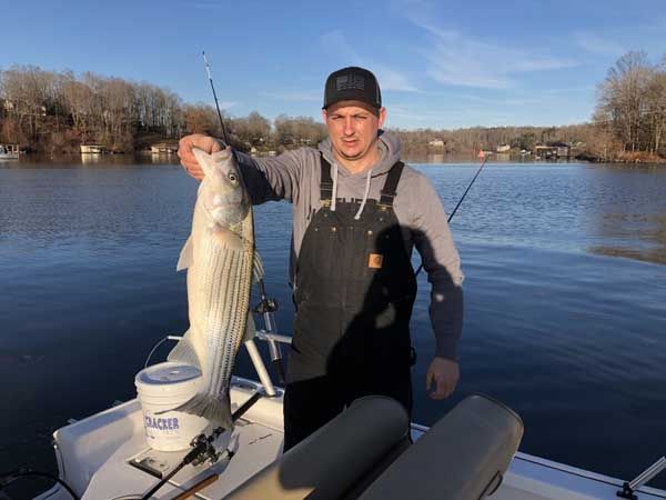 Man holding a large fish on a boat on a calm lake with trees in the background