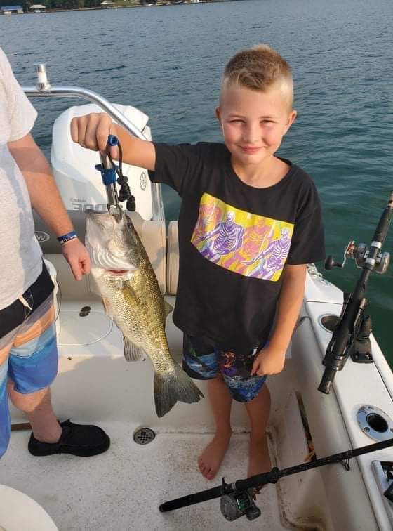 Boy on a boat holding a large fish beside fishing rods on the deck