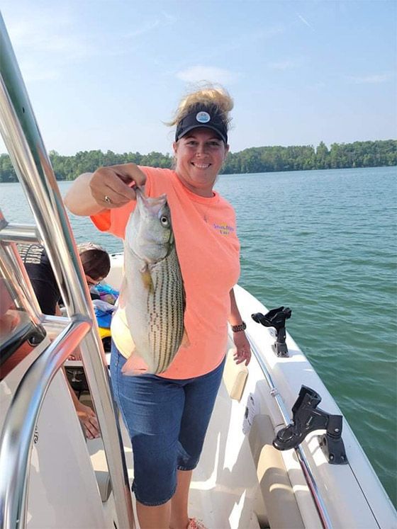 Person on a boat holding up a large striped fish on a sunny lake