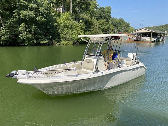 White fishing boat cruising on a green river beside trees and a dock
