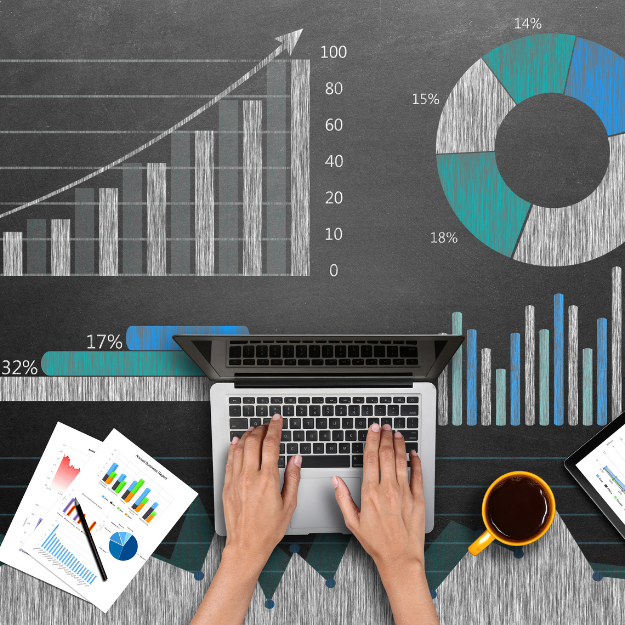 A person is typing on a laptop in front of graphs