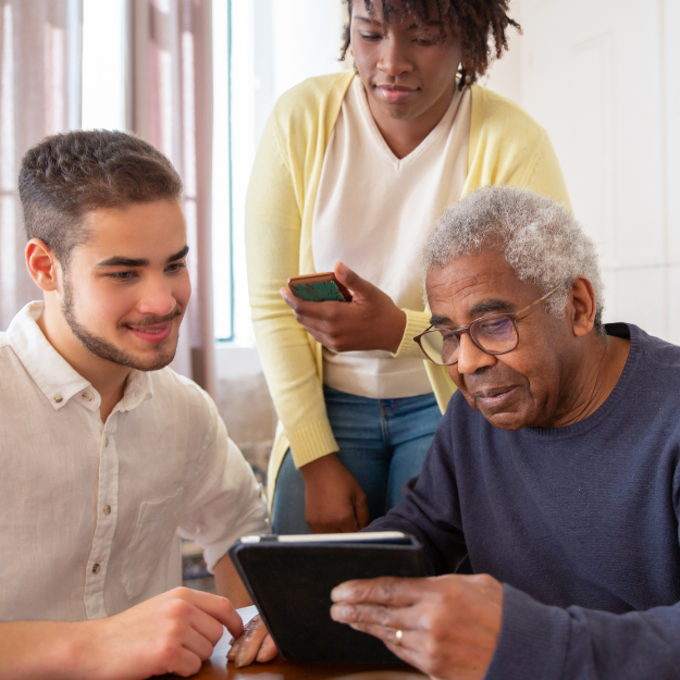 A group of people are sitting around a table looking at a tablet.