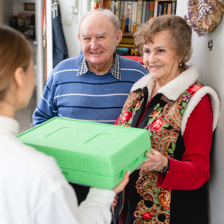 A woman is holding a green box in front of a man and woman
