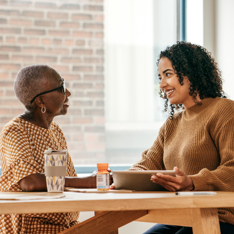 Two women are sitting at a table talking to each other.