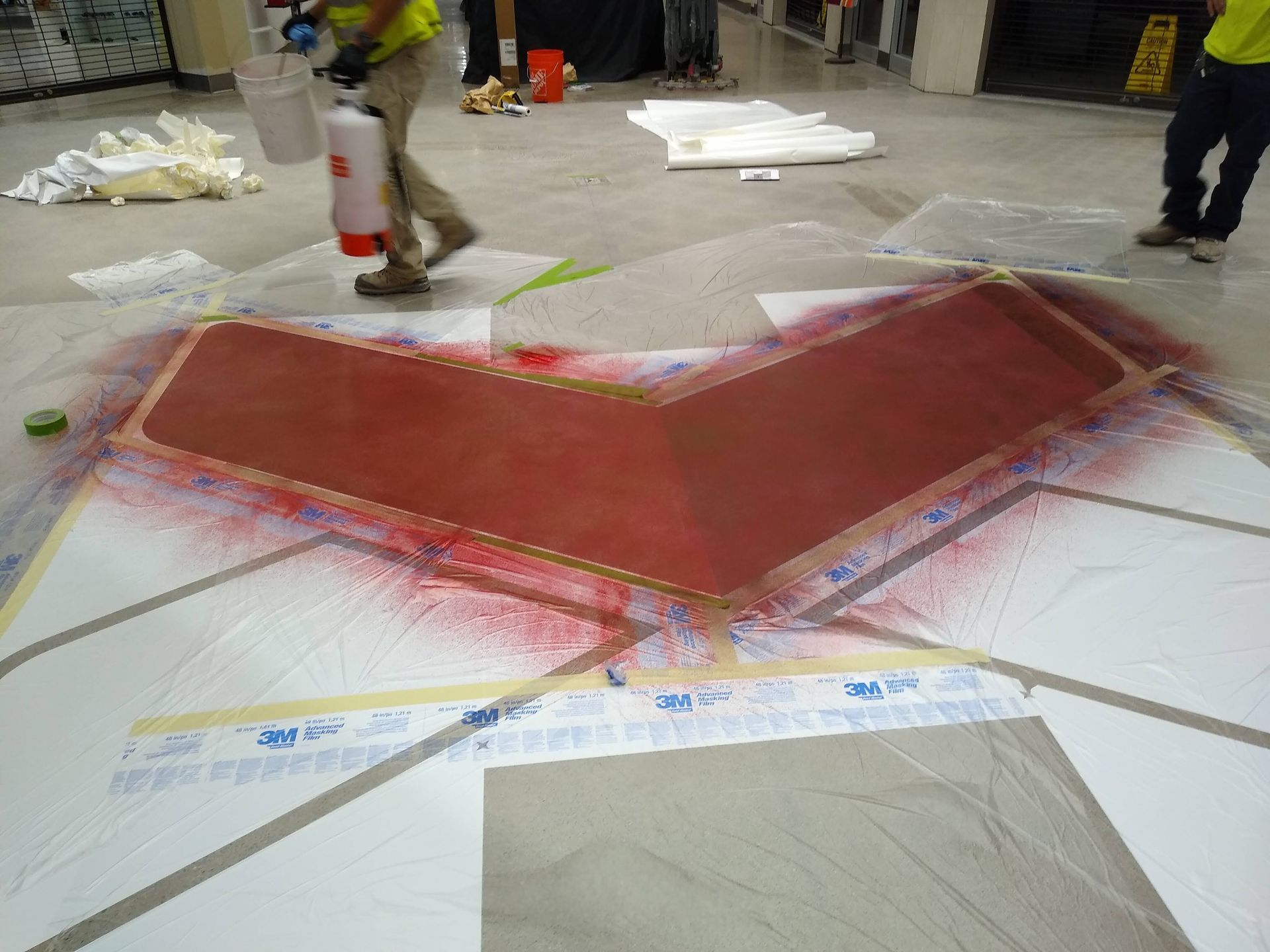 A man is spray painting a red arrow on the floor.
