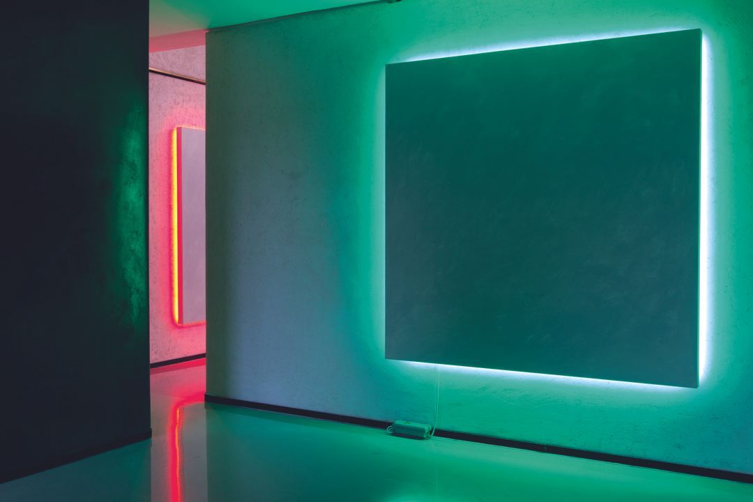 Stanza moderna con pannelli a parete luminosi al neon che riflettono tonalità turchesi e rosa.