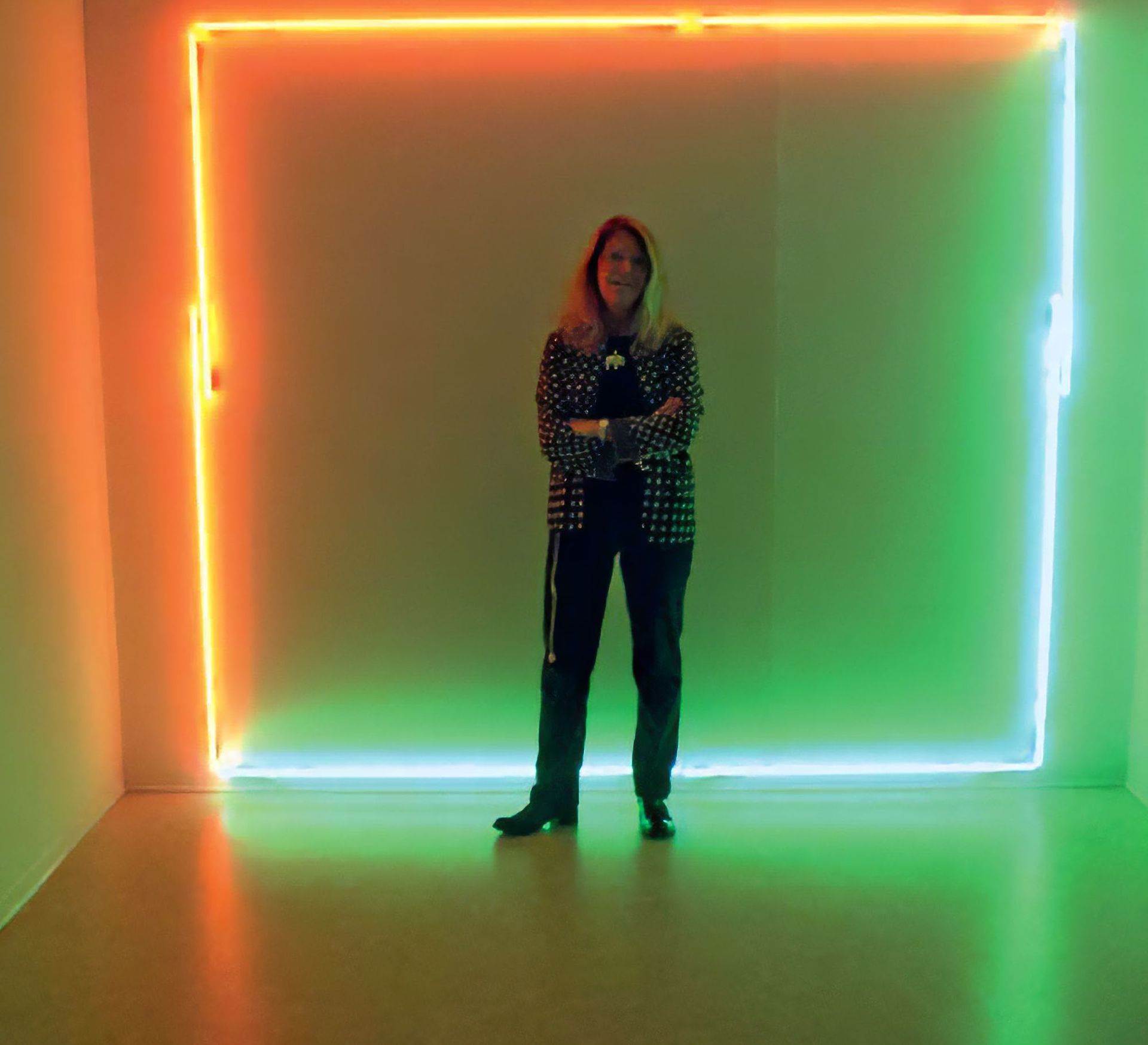 Persona in piedi in una galleria accanto a un'installazione quadrata luminosa al neon nei colori arancione, verde e blu.
