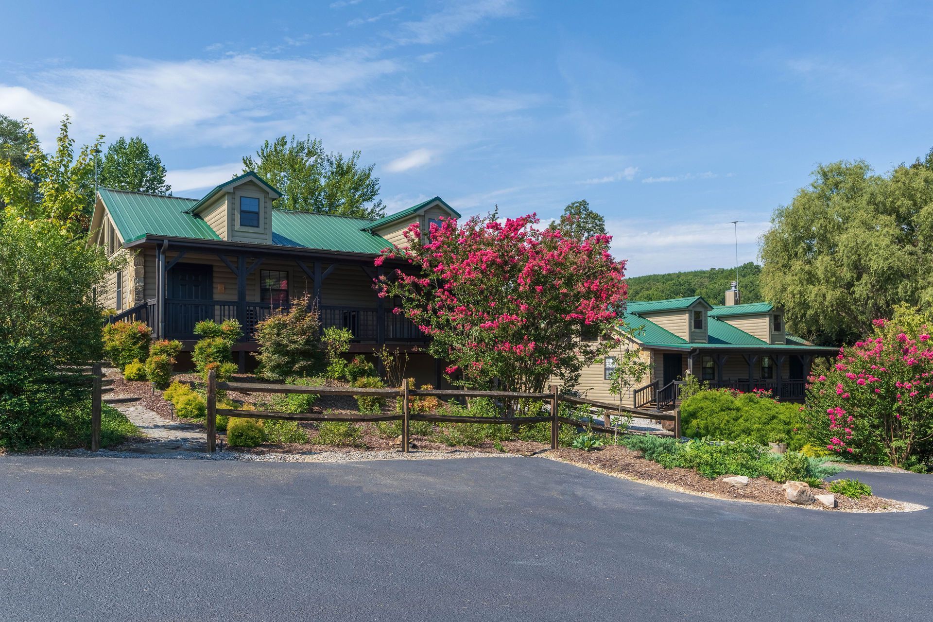 Cabin-style house with green roof, brown siding, and landscaped yard. Driveway in front.
