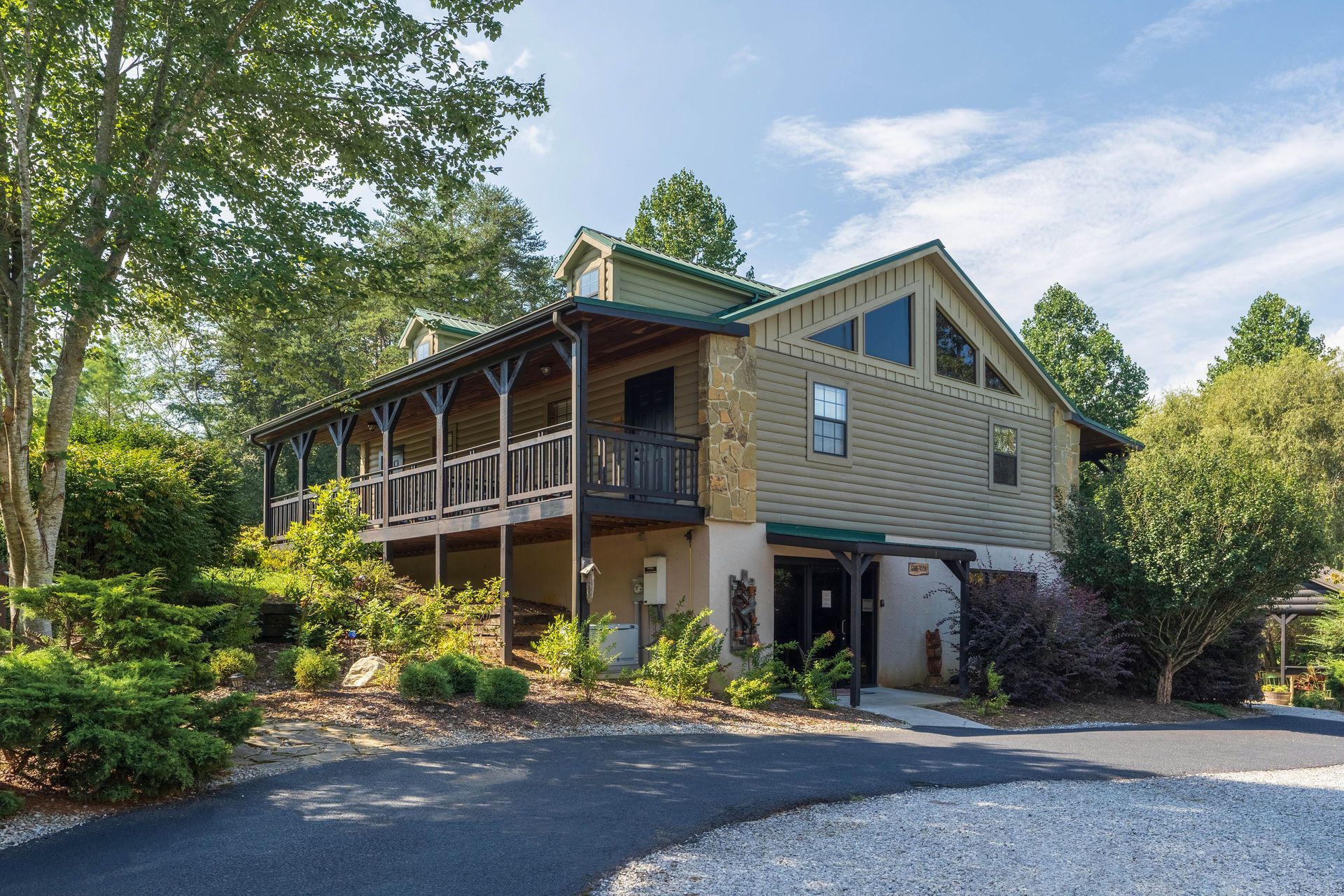 Two-story house with wrap-around porch, gravel driveway, and surrounding trees.