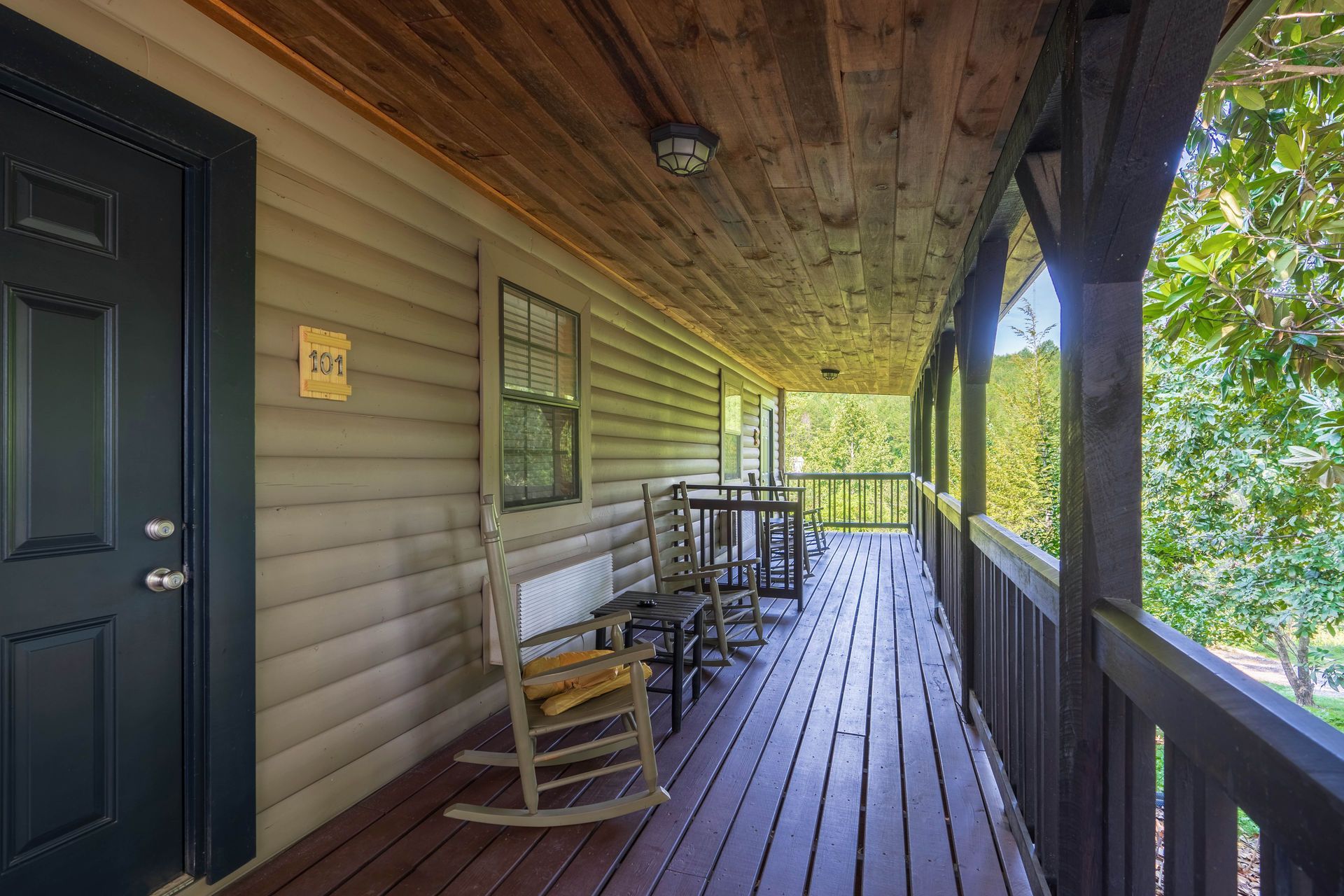 A cabin porch with a black door, rocking chair, and a table with chairs.