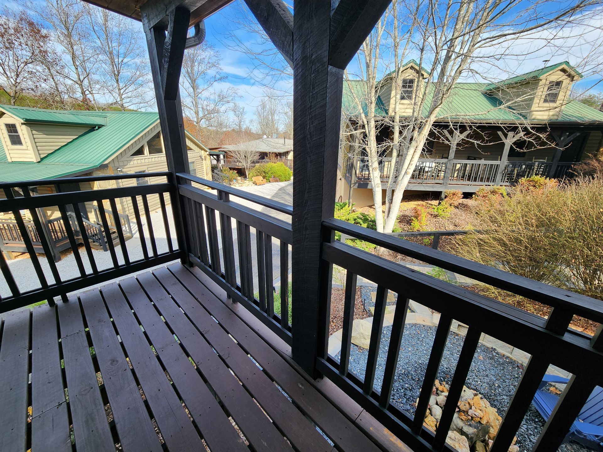 Wooden balcony with dark railing overlooking buildings with green roofs. Sunny day.