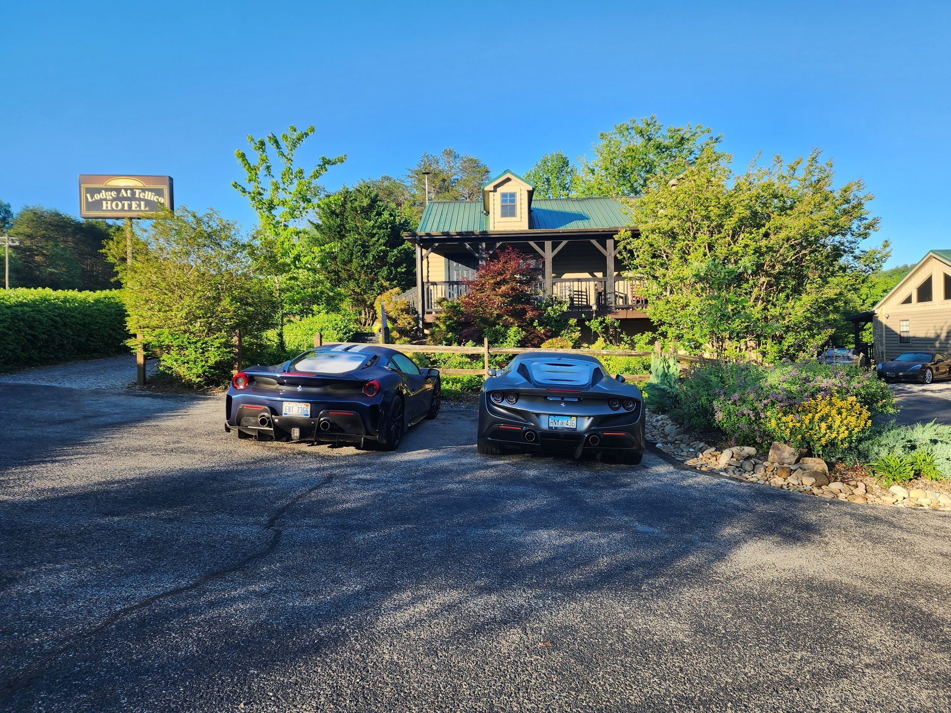 Two dark sports cars parked in front of a wooden cabin. Sign above reads 