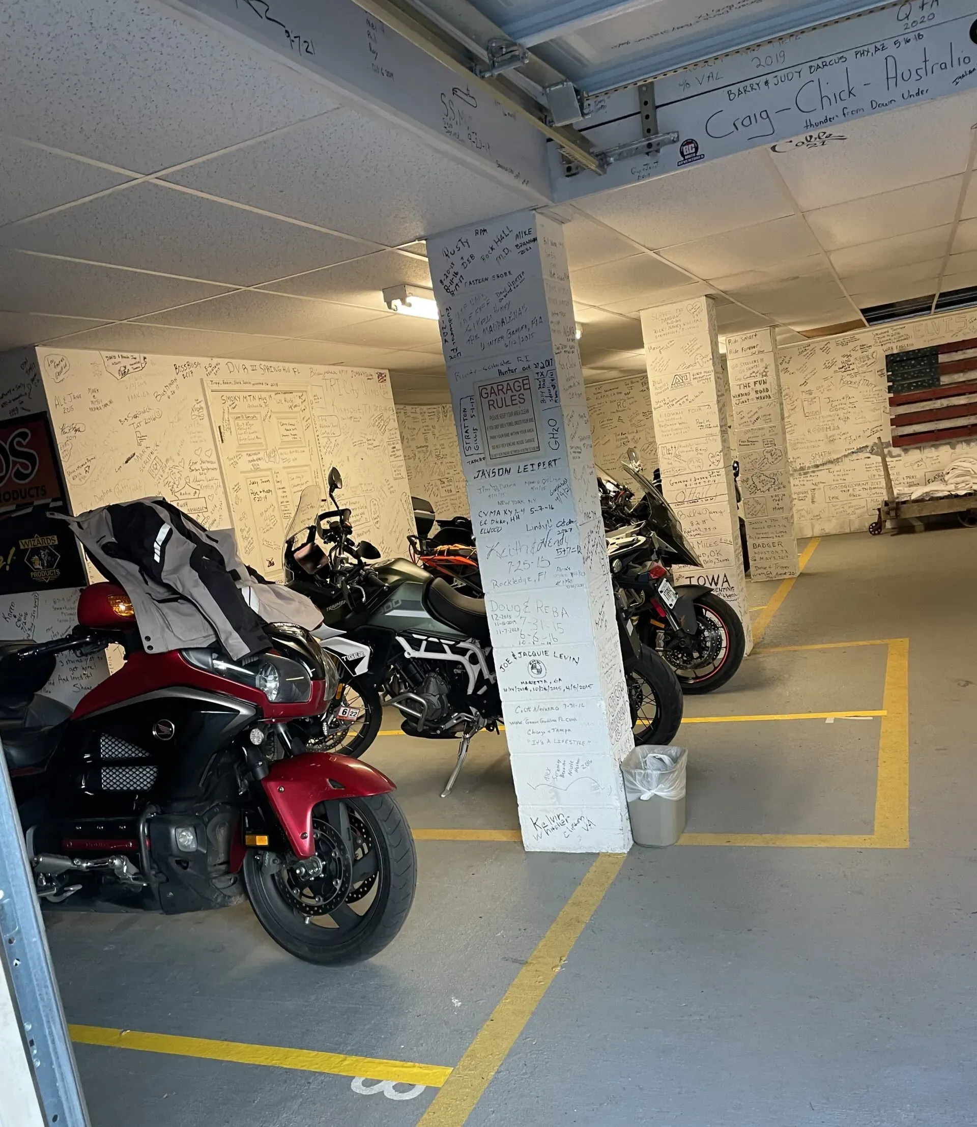 Motorcycles parked in a garage with painted walls. Red, black, and green bikes in marked spaces.