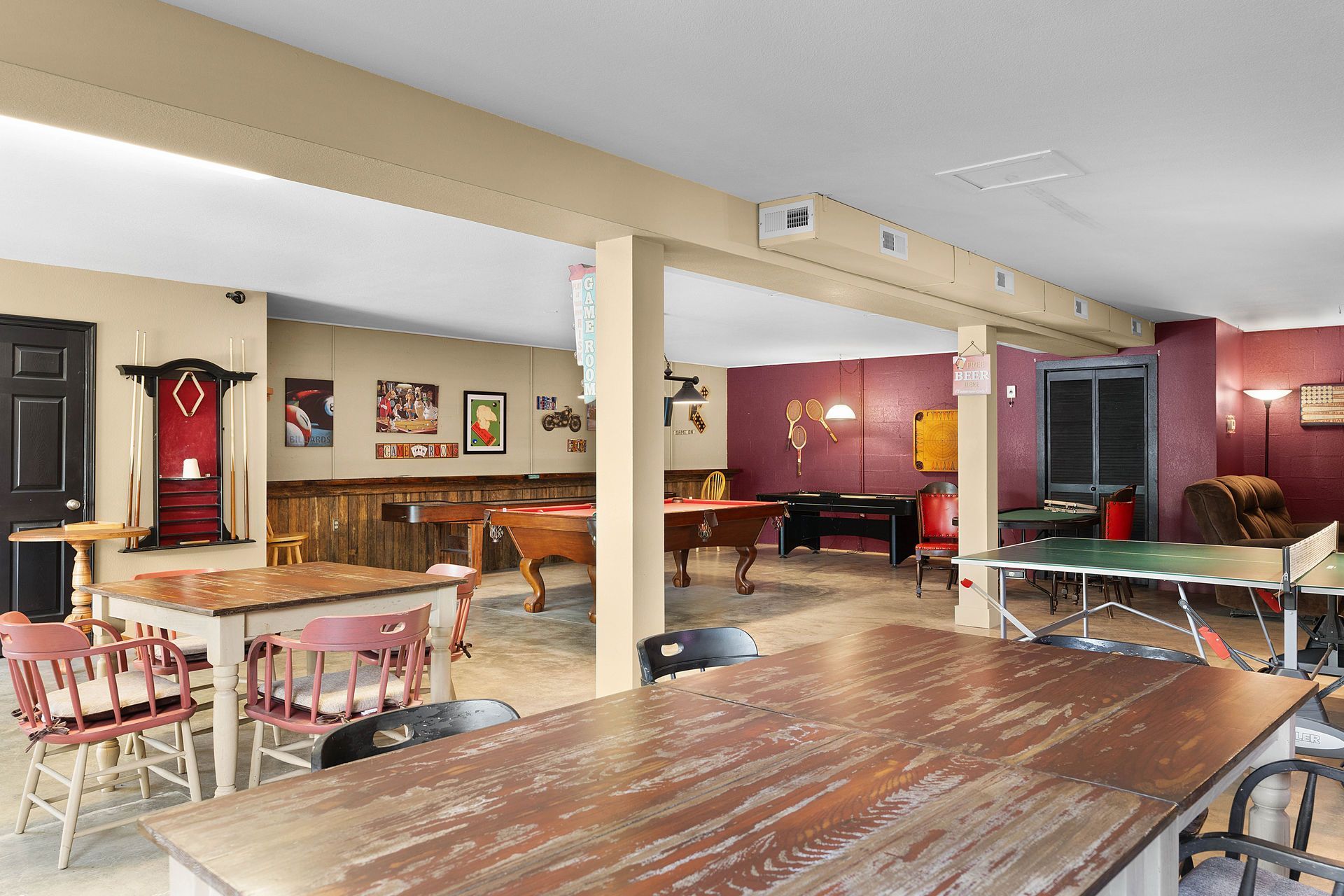 Game room with pool tables, a ping pong table, and seating. Beige and red walls, wood accents.