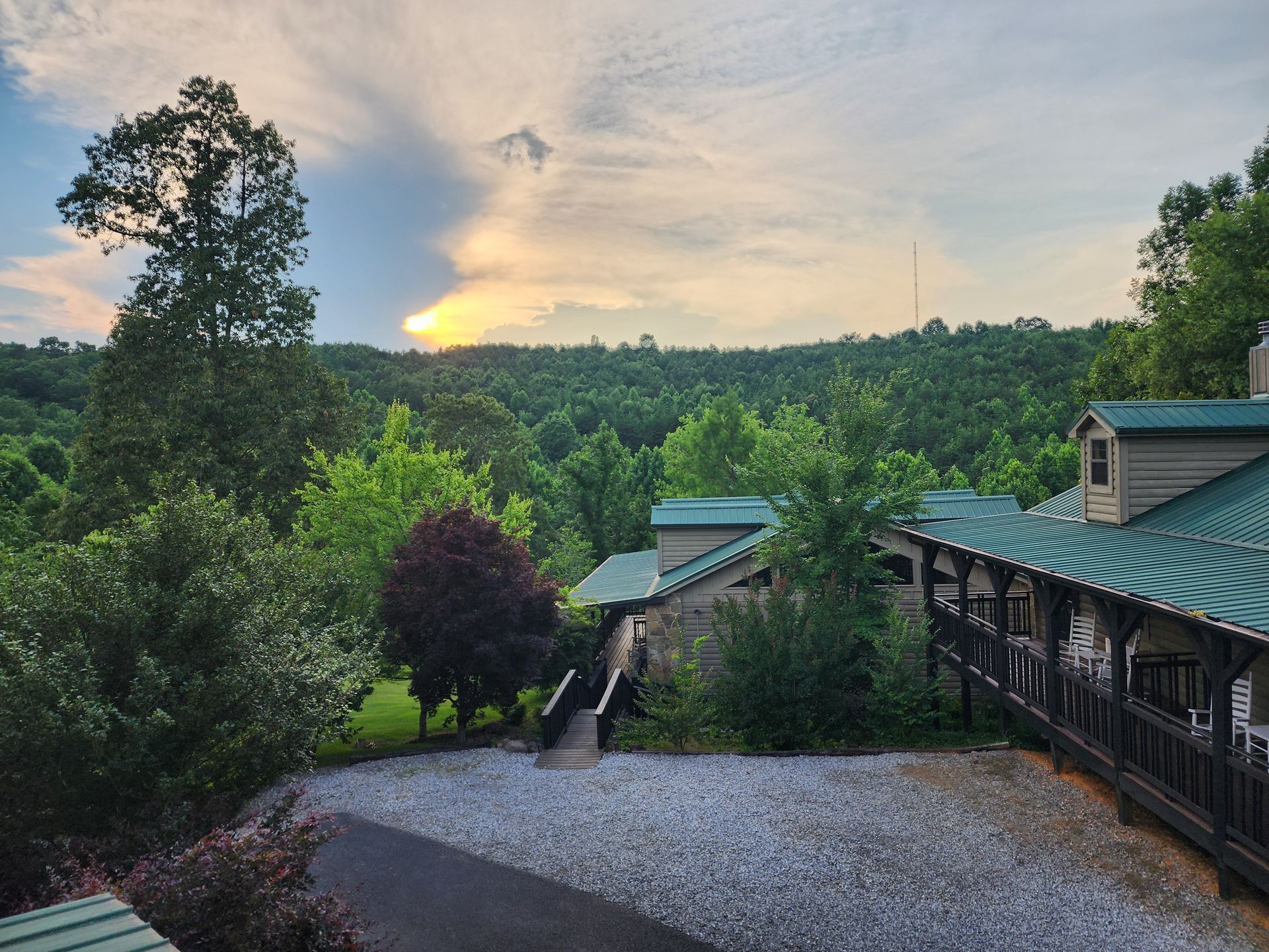 Sunset over a forested mountain with a building in the foreground, green roofs, and a walkway.