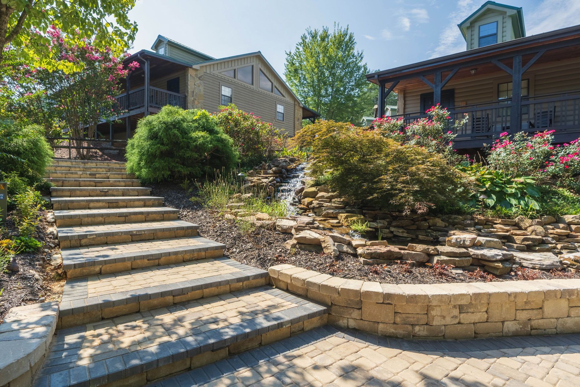 Stone steps lead up to wooden buildings, surrounded by landscaping, trees, and small waterfall.